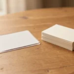A generic plastic gift card lying next to a small folded stack of paper currency on a plain wooden surface, no text, no numbers, no real person's hands or face