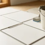 Close view of a freshly grouted gray tile floor with a grout float, a mixing bucket, and a bag of grout powder, no people present