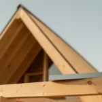 A spirit level and tape measure resting on a sloped asphalt shingle roof under a clear sky, no people present