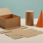 A cardboard box unfolded into a flat net beside a cylinder, a cone, and a ball on a desk with a ruler and a notepad
