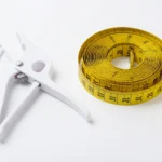 Skinfold calipers and a soft measuring tape resting on a plain surface, representing at-home body fat measurement, no text-in-image, no real person