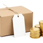 A price tag attached to a product beside a small stack of coins, representing pricing a product for profit, no text in image