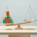 A balance scale tipped to one side with a taller stack of colored blocks on the lower pan, on a light desk