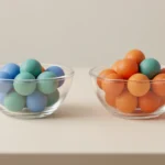 Two small glass bowls of colored marbles side by side on a light desk, one slightly fuller, suggesting a comparison between samples