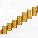 A rising staircase of coin stacks growing taller with each step, representing retirement savings targets that increase with age