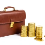 A briefcase beside a stack of gold coins with one slice lifted away, representing self-employment tax taken from earnings, no text in image